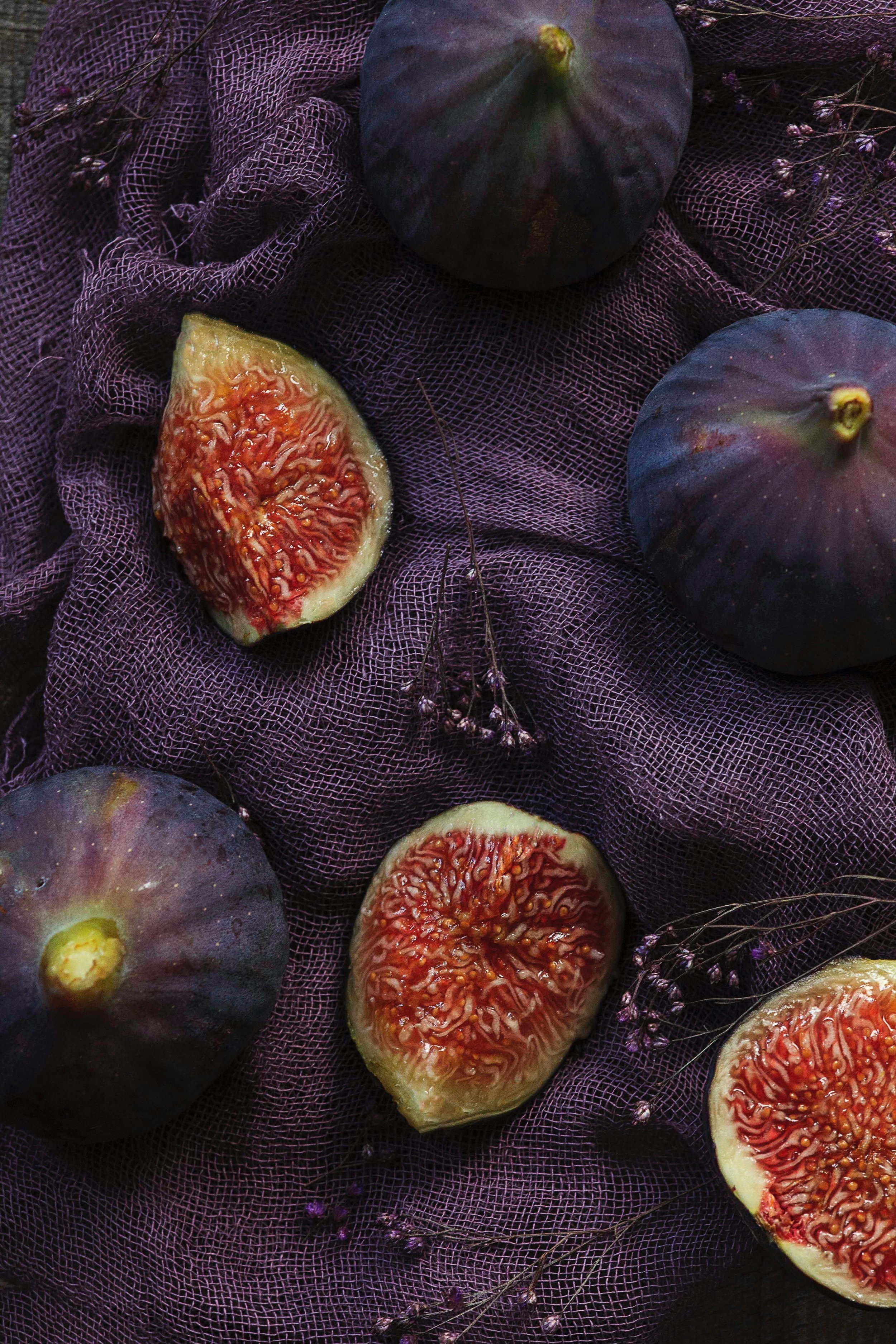 Whole and halved figs arranged on a deep purple muslin cloth with sprigs of dried lavender and baby's breath