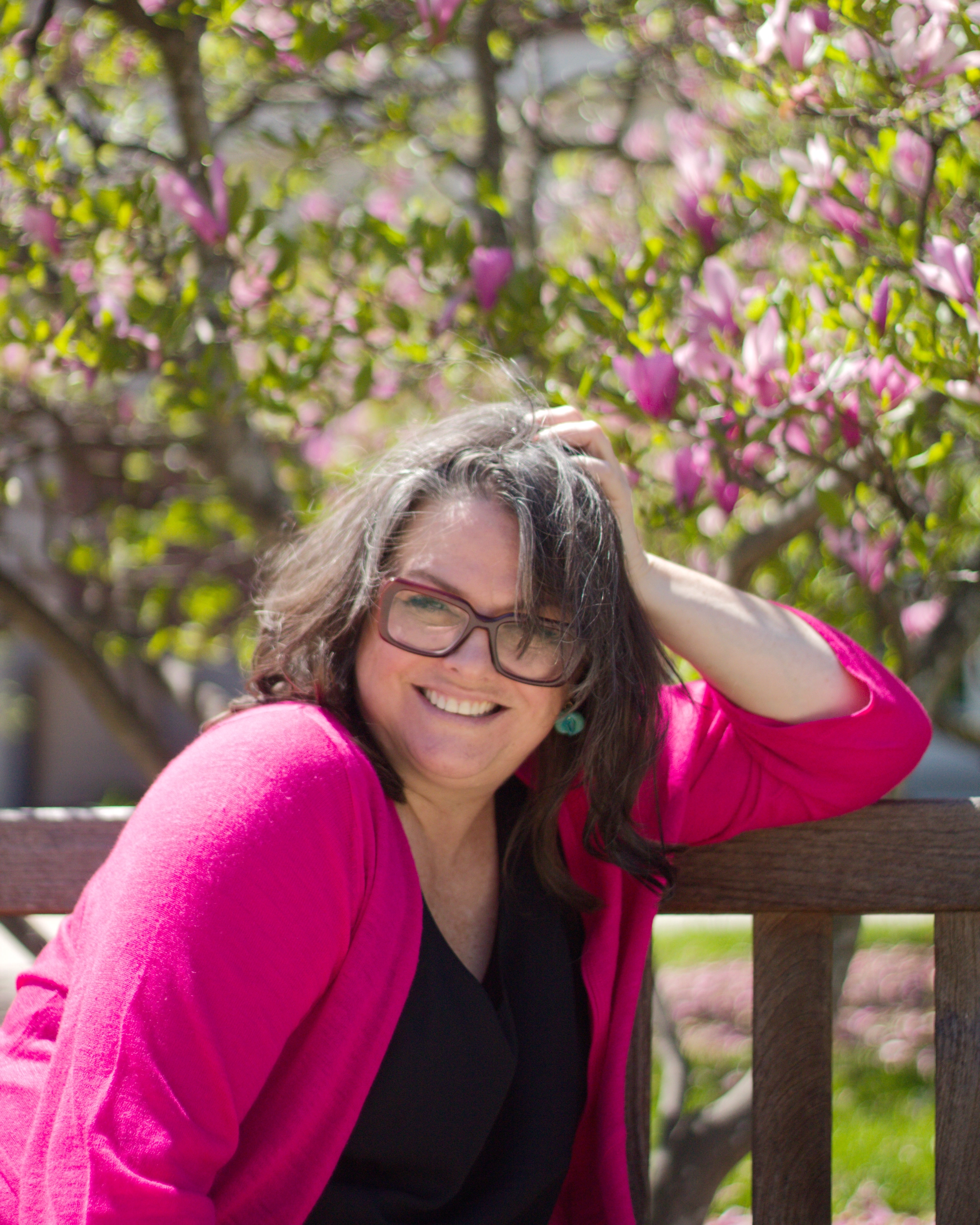 Heather, kuladoula founder, seated by a wooden bench in front of a magnolia tree in full pink bloom