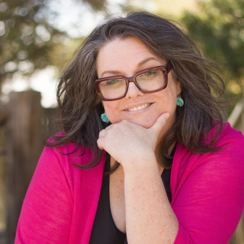 Heather, kuladoula founder, smiling warmly with her hand resting at her chin, glasses, soft outdoor light
