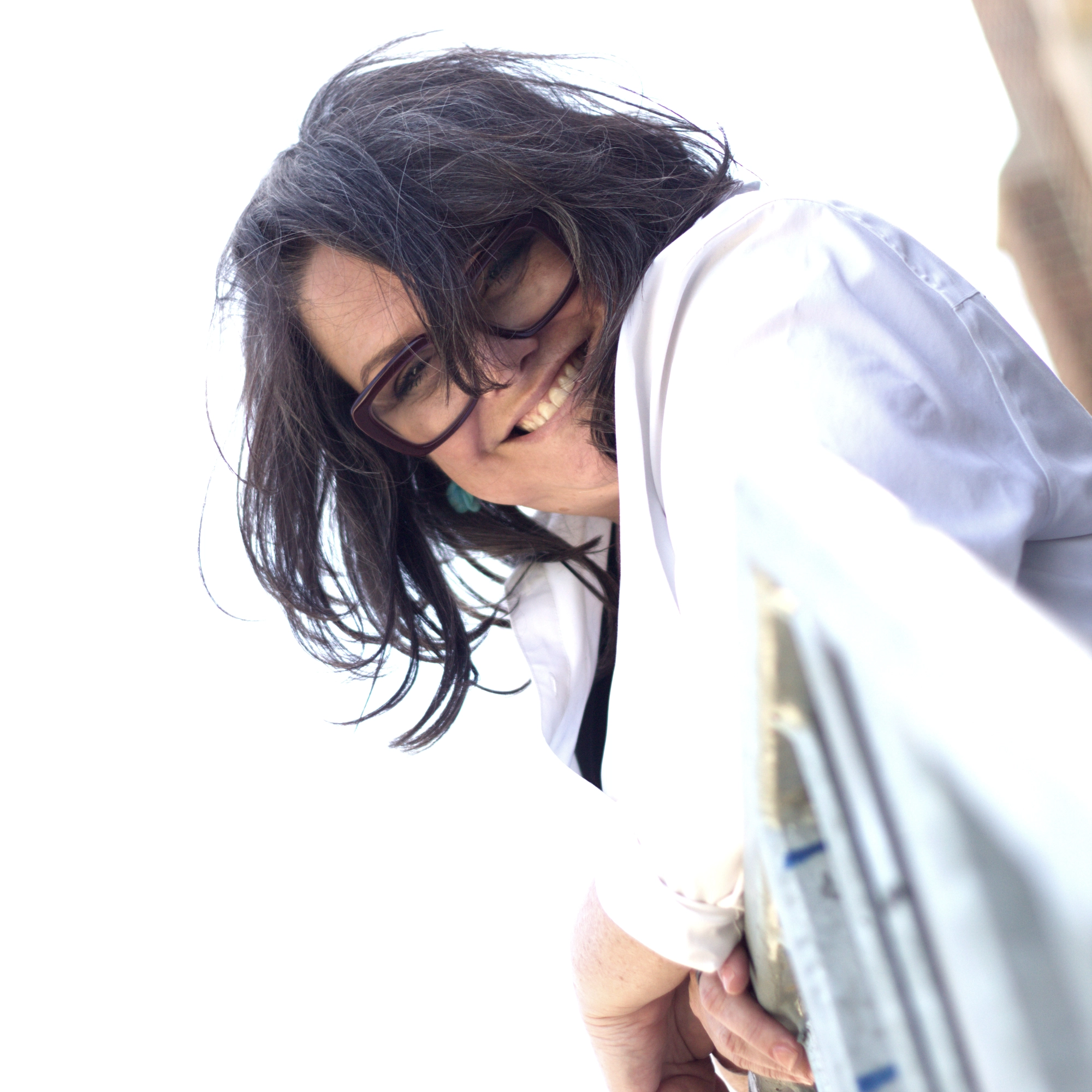 Heather peeking playfully over a metal railing, head tilted, hair flowing, smiling